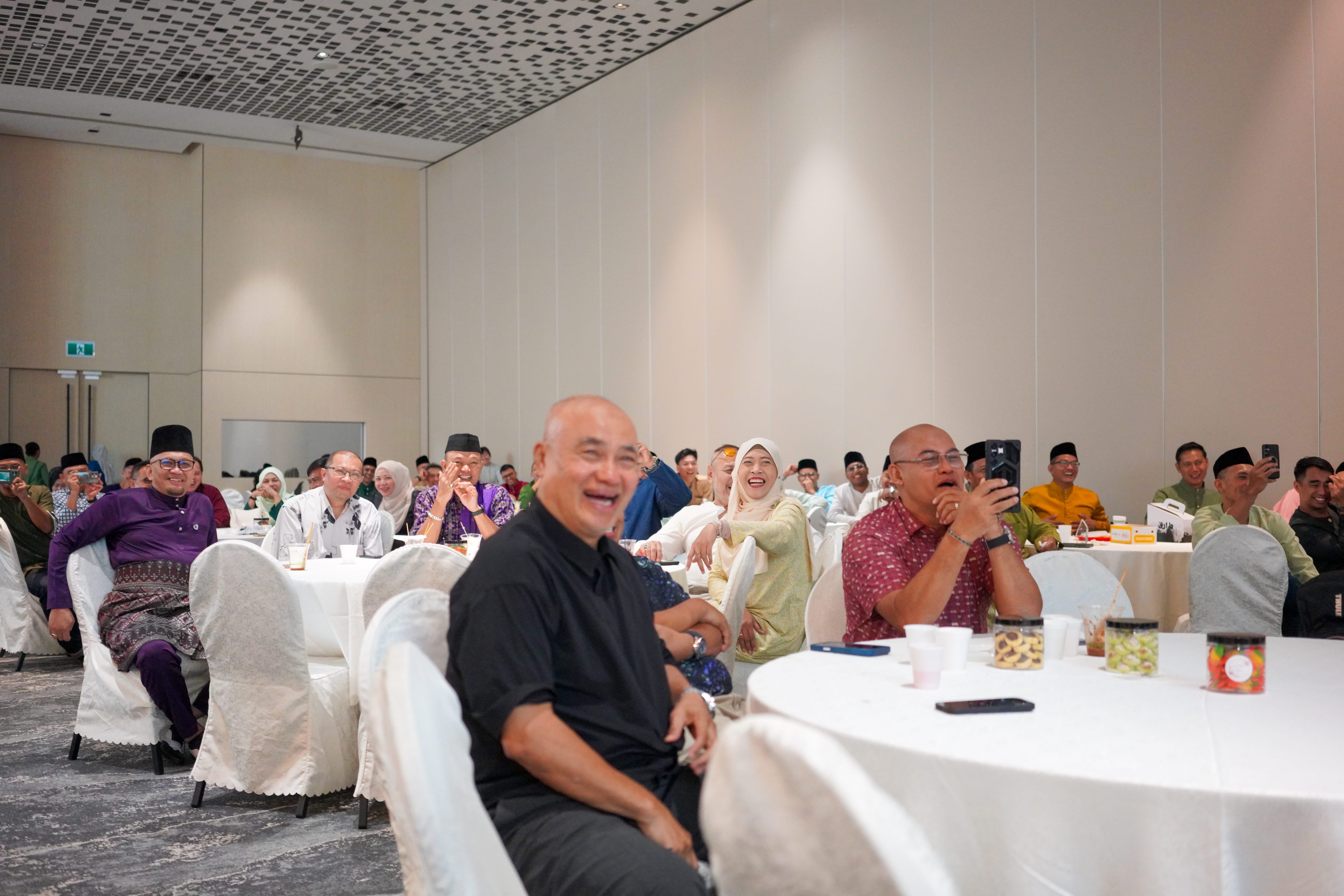 Guests laughing and reacting to a comedy performance while seated around banquet tables in the function hall.